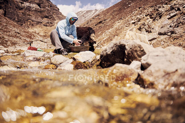 Trekker lavando su ropa junto al arroyo en Nepal - foto de stock