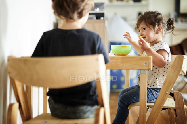 Menina bonito olhando para o irmão enquanto tomando café da manhã em casa — Fotografia de Stock