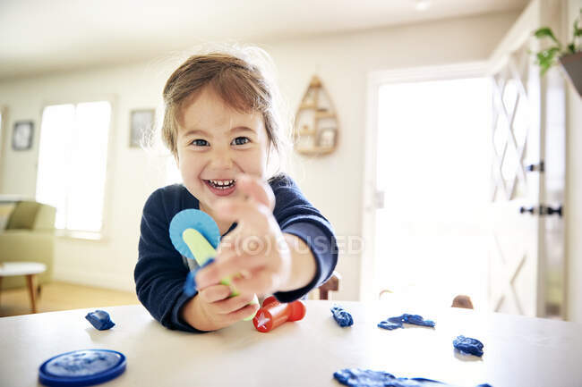 Retrato de menina alegre brincando com brinquedos na mesa em casa — Fotografia de Stock