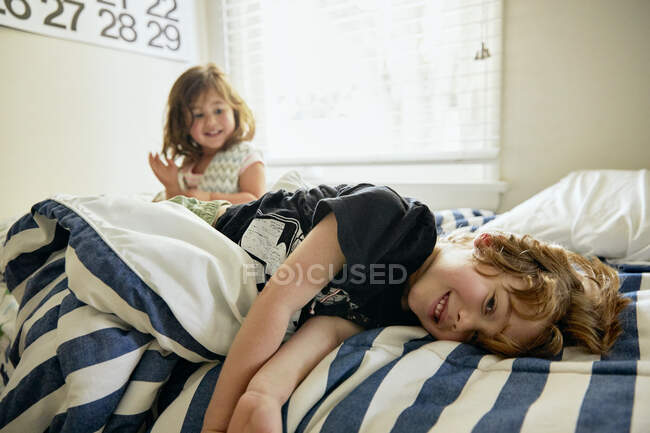 Портрет усміхненого хлопчика лежачого сестри на ліжку у спальні. — стокове фото