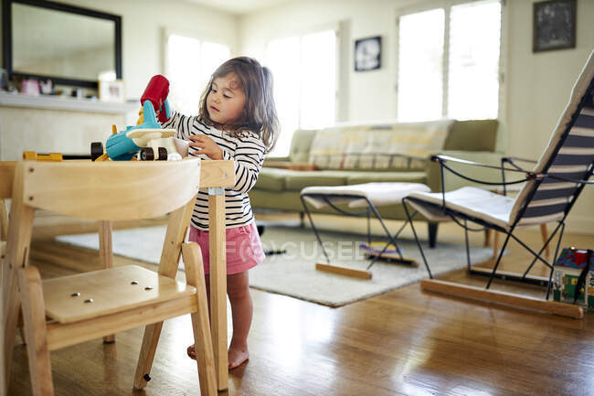 Милая девушка играет с игрушками на столе в гостиной на дому — стоковое фото
