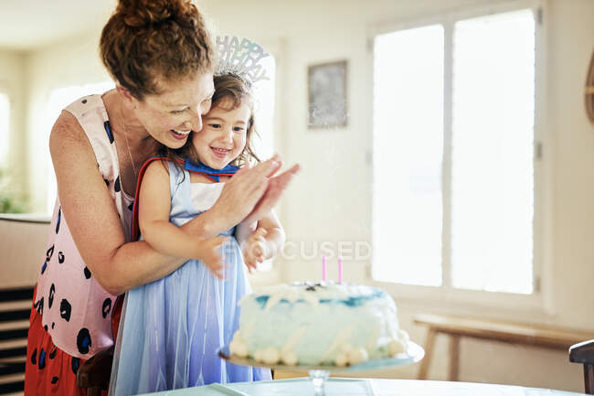 Feliz madre aplaudiendo mientras celebra el cumpleaños de su hija en casa - foto de stock