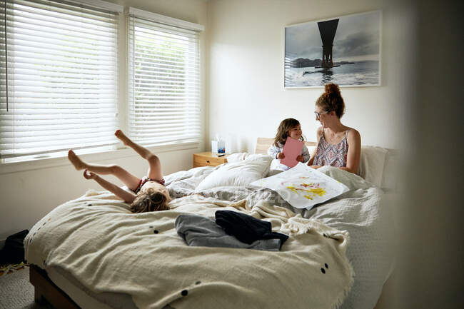 Hija dando tarjeta de felicitación a la madre en la cama en casa - foto de stock