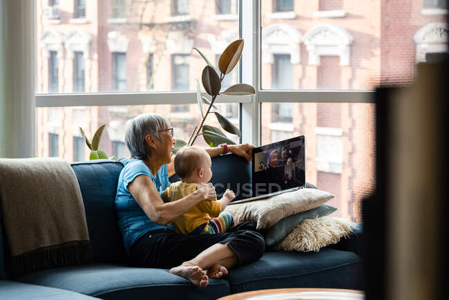 Grandmother and grandaughter using laptop to video chat with relatives — Stock Photo