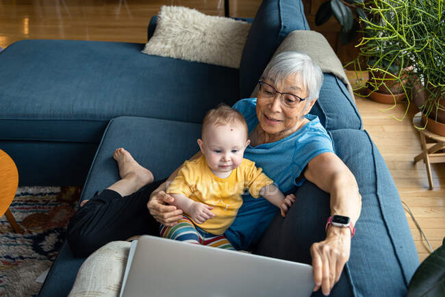 Бабуся сидить з онукою, використовуючи ноутбук для відеодзвінків — стокове фото