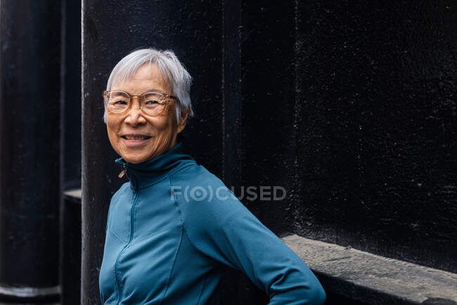Smiling senior woman wearing eyeglasses standing by black wall — Stock Photo