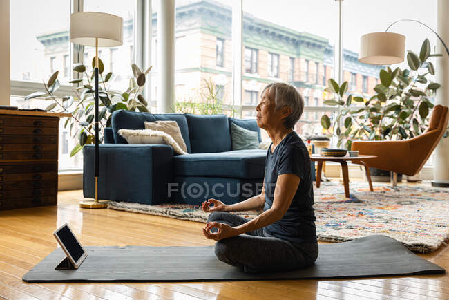 Mulher sênior meditando enquanto aprende através de tablet digital na sala de estar em casa — Fotografia de Stock