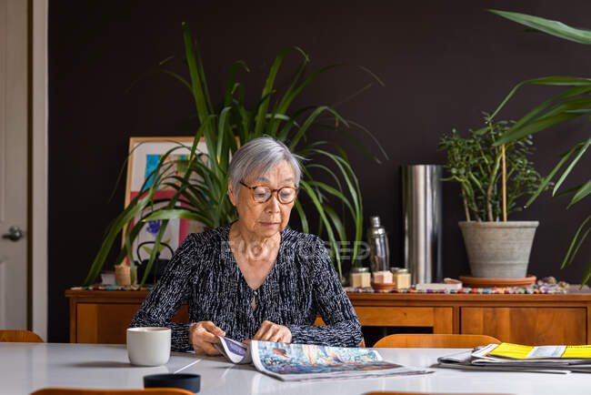 Donna anziana che legge il giornale mentre siede a tavola con il caffè — Foto stock