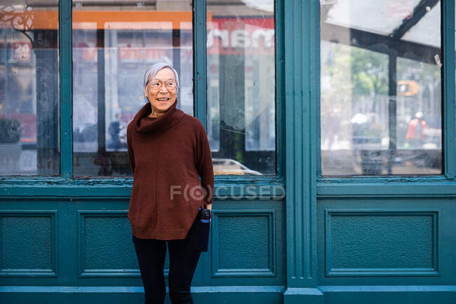 Щаслива старша жінка дивиться геть, стоячи навпроти стіни — стокове фото