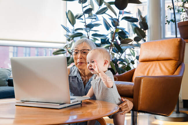 Senior woman sitting with granddaughter using laptop to video call — Stock Photo