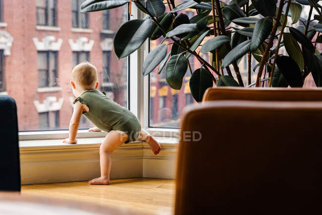Curious toddler baby girl looking out of window in city — Stock Photo