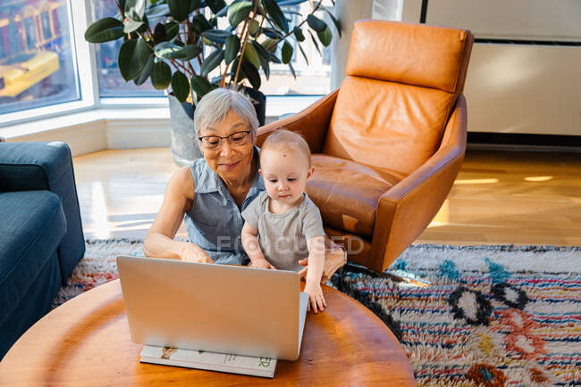 Donna anziana seduta con nipote che fa videochiamate su laptop — Foto stock