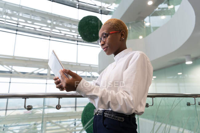 Preto feminino gerente inclinado no corrimão e usando tablet durante o trabalho no escritório — Fotografia de Stock