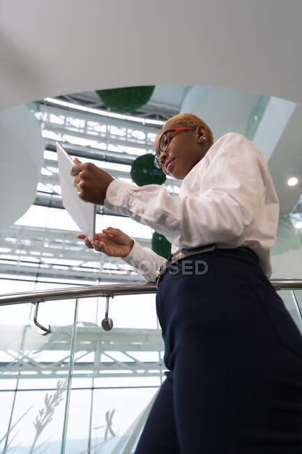 Jeune femme afro-américaine en vêtements décontractés intelligents en utilisant la tablette dans le bureau moderne — Photo de stock