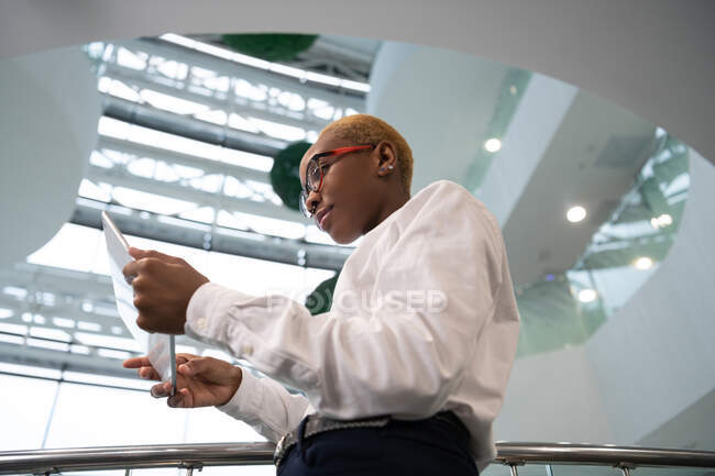 Impiegata nera in occhiali navigando tablet digitale durante il lavoro in ufficio moderno — Foto stock