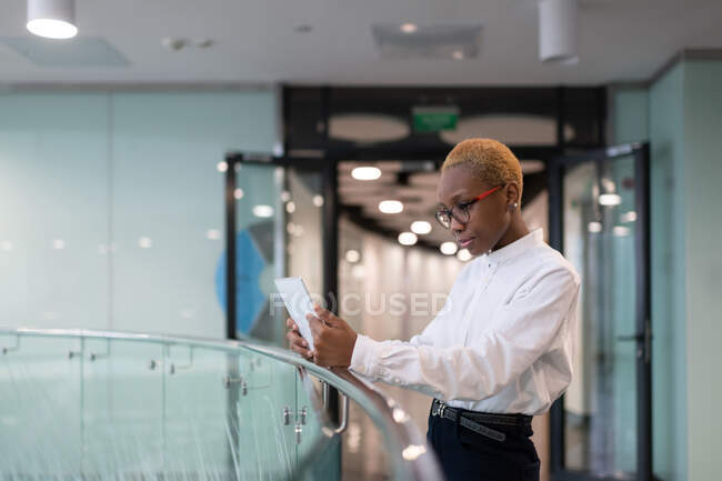African American worker reading data on digital tablet in hallway of modern office — Stock Photo