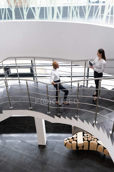 Diverse young female colleagues meeting on steps and talking during work in office — Stock Photo