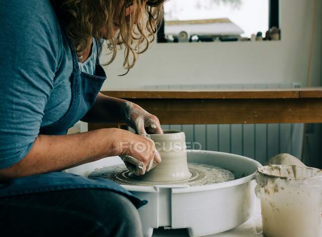 Mujer modelando arcilla en una rueda de cerámica en un estudio en el Reino Unido - foto de stock