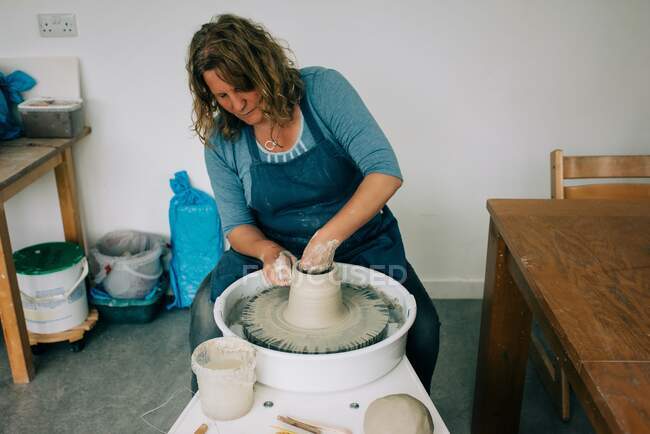 Жінка зосереджена на обертанні глини на гончарному колесі в домашній студії — стокове фото