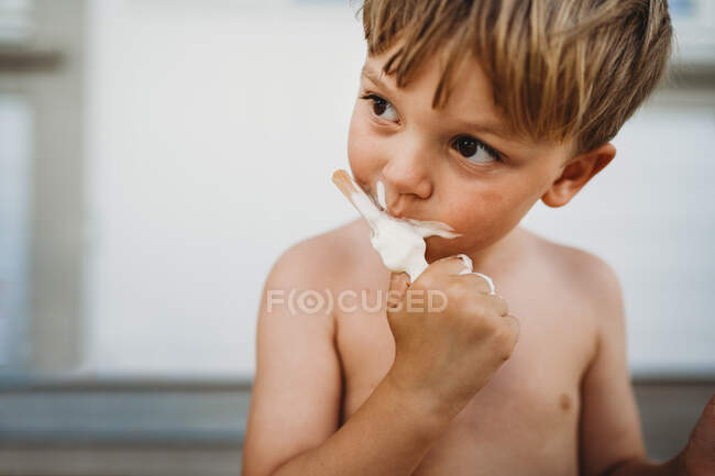 Милий молодий хлопчик їсть морозиво, дивлячись на бік влітку — стокове фото