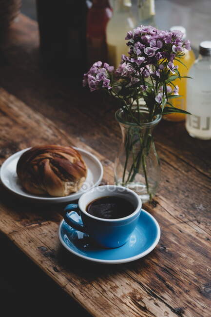 Cup of coffee and flowers with bun on wooden table — Stock Photo