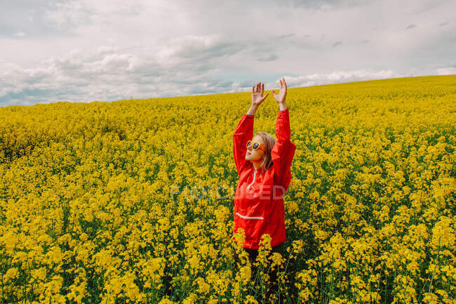 Blonde in sunglasses and red tracksuit in rapeseed field — Stock Photo