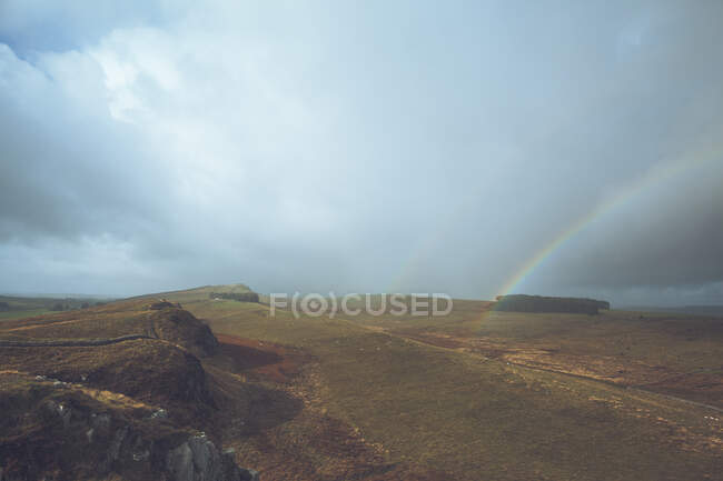 Бесконечный пейзаж наполнен яркими радугами в небе в то время как у Стены Адриана в Великобритании. — стоковое фото