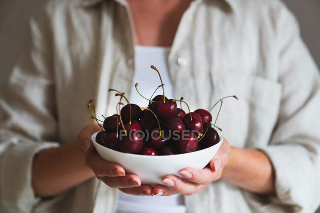 Donna che tiene una ciotola di ciliegie mature fresche in cucina — Foto stock