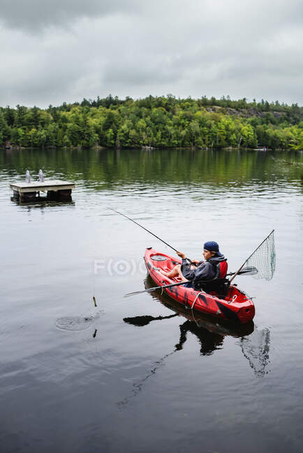 Adolescente ragazzo pesca in kayak su un lago in una giornata estiva. — Foto stock