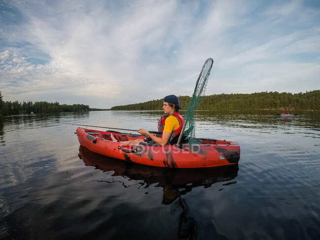 Adolescente ragazzo pesca in kayak su un lago in una giornata estiva. — Foto stock