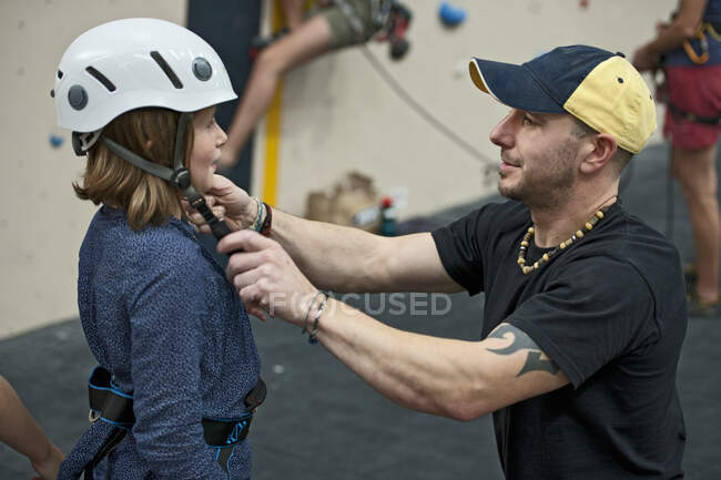 Climbing coach helping girl adjusting climbing helmet — Stock Photo