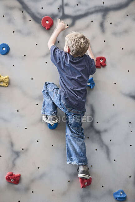 Jeune garçon escalade sur mur de bloc intérieur — Photo de stock