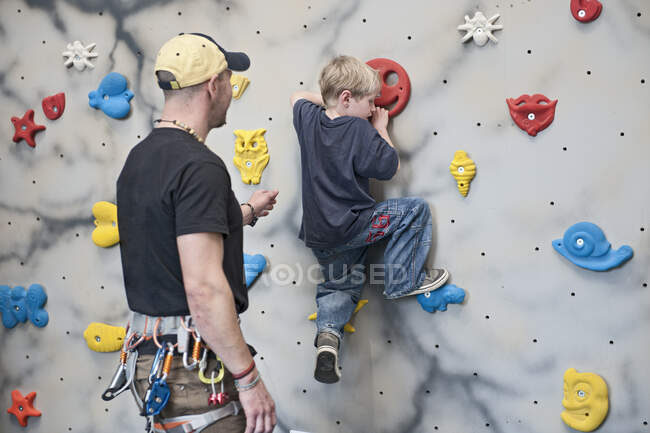 Entraîneur d'escalade aider jeune garçon sur mur de blocs — Photo de stock