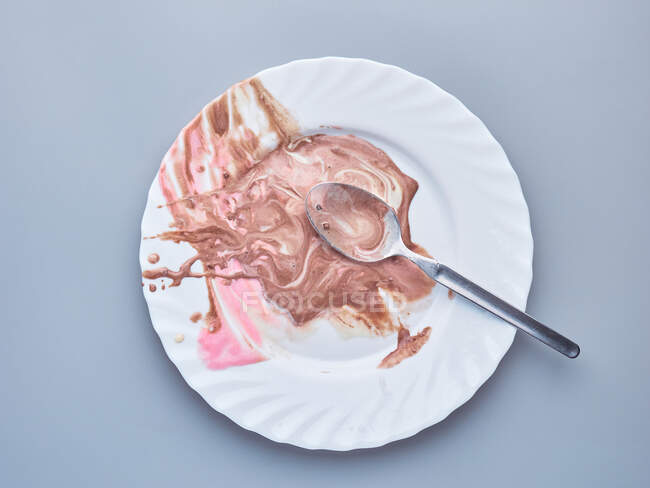 Une assiette blanche avec une cuillère et des restes de crème glacée, isolés sur un fond clair — Photo de stock