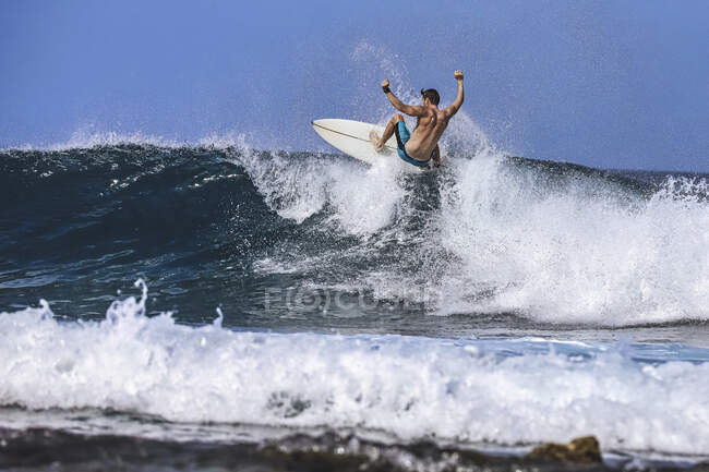 Hombre con tabla de surf surfeando en la ola del mar contra el cielo despejado - foto de stock