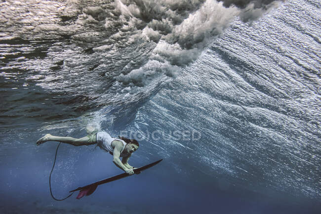 Сёрфер-мужчина держит доску для сёрфинга во время погружения под водой на Мальдивах — стоковое фото
