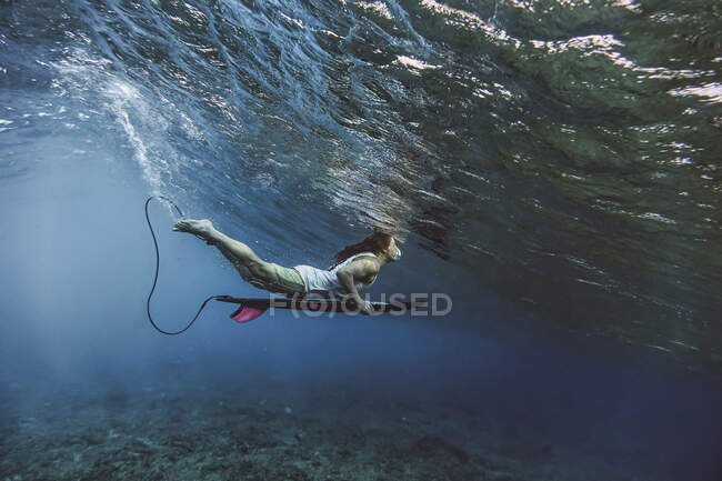Сёрфер-мужчина держит доску для сёрфинга во время погружения под водой на Мальдивах — стоковое фото
