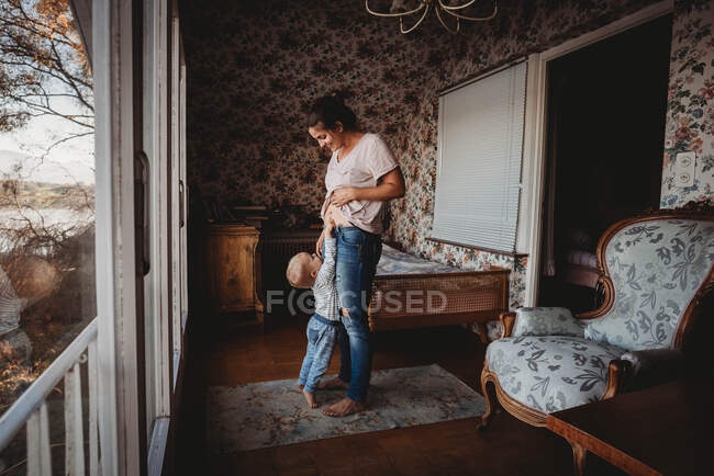 Toddler touching mom's belly in vintage room with wallpaper — Stock Photo