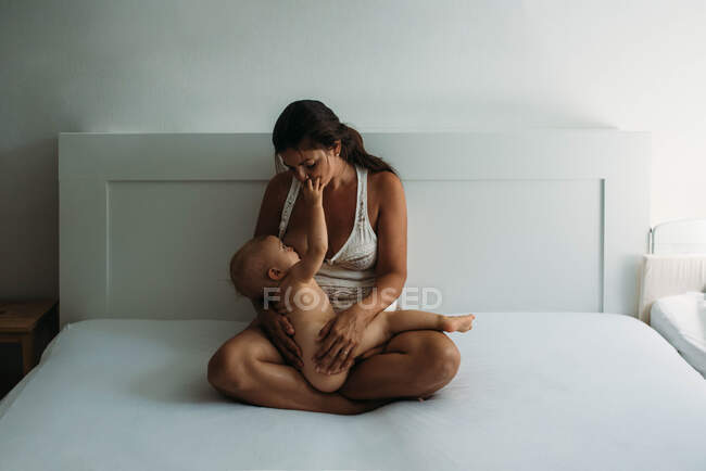 Mom breastfeeding while naked baby touches her face in bedroom — Stock Photo