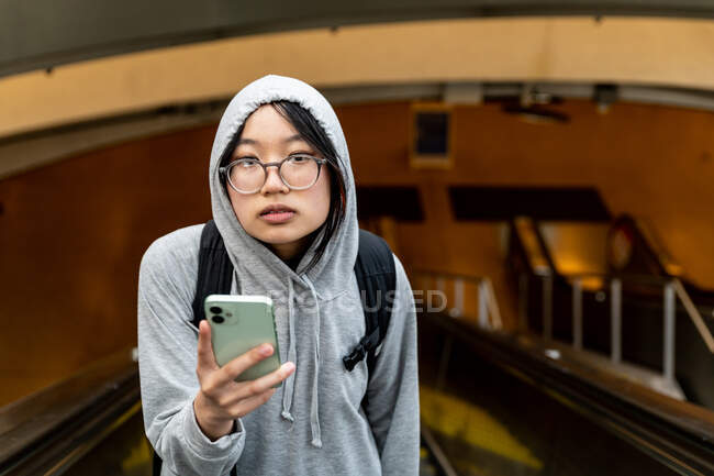Молода жінка тримає мобільний телефон, що виходить з залізничної станції, виглядає втомленою — стокове фото