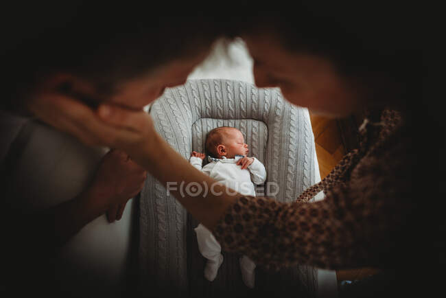 Мама з татом тримаються за руки і дивляться, як спить новонароджене дитя. — стокове фото