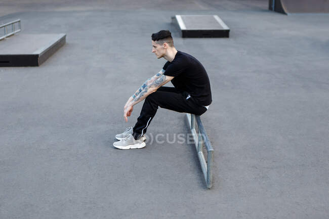 Joven morena hombre sentado solo en un asfalto skate parque infantil - foto de stock