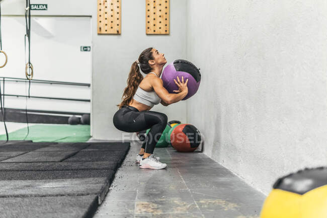 Mulher fazendo Wall Ball Shot em posição de agachamento no ginásio fazendo crossfit — Fotografia de Stock