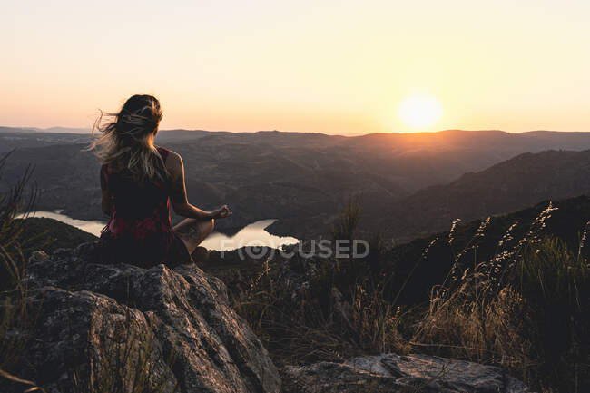 Una mujer sentada en posición de meditación de loto en una hermosa puesta de sol. - foto de stock