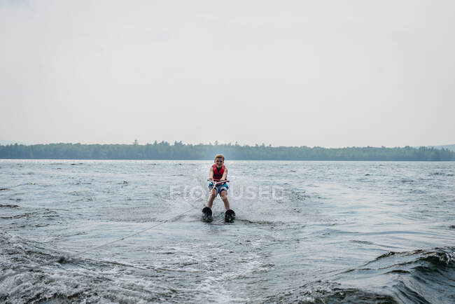 Tween menino esqui aquático no lago com árvores no fundo — Fotografia de Stock