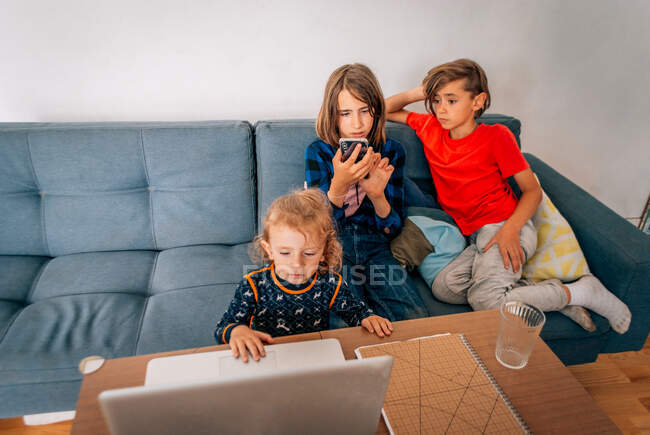 Drei Kinder sehen Cartoons und spielen mit Handy und Laptop — Stockfoto