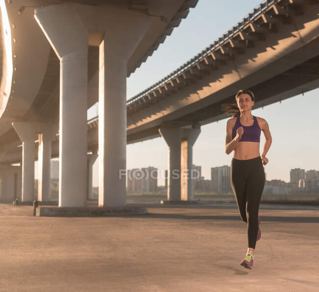 Fit female jogger running under bridge during fitness training on city street — Stock Photo