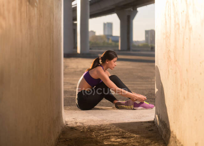Спортсмен завязывает шнурки на кроссовках, сидя возле переулка перед тренировкой — стоковое фото