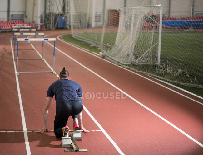 Athlète masculin se préparant à faire course de barrière à partir de la position de départ accroupi sur les blocs — Photo de stock