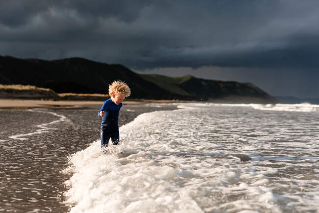 Criança de cabelos encaracolados brincando em ondas na praia na Nova Zelândia — Fotografia de Stock